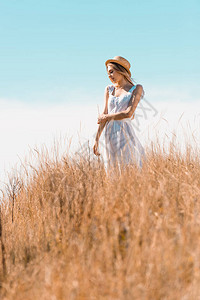 身着白衣和草帽的年轻女子在站草丘上时视而不见图片