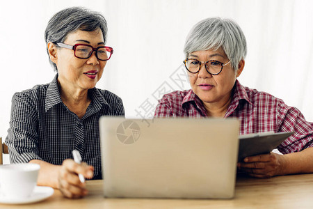 两个朋友快乐的老年亚洲老年妇女在家中微笑和使用笔记本电脑的肖图片