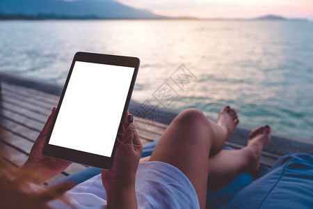 一个女人用黑色平板纸Pc与空白的桌面屏幕在蓝天空背景的海边图片