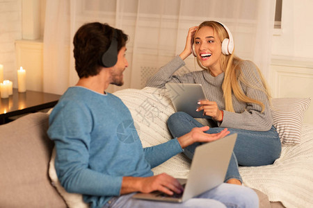 快乐配偶使用笔记本电脑和数字平板电脑戴耳机在晚上回家后放松图片