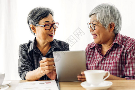两个朋友快乐的老年亚洲老年妇女在家里微笑和使用数字平板电脑工作的肖图片
