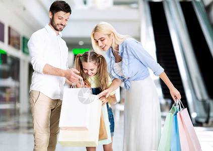 成功的家庭购物男人展示多彩的沙袋买东西给他的妻子和女儿在购物中站图片