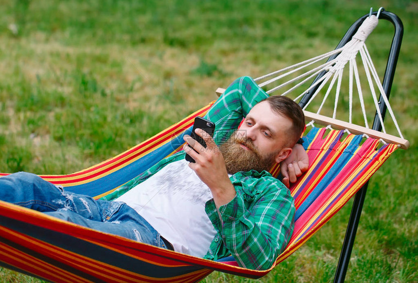 男人用手机上的一个应用程序在吊床上挥图片