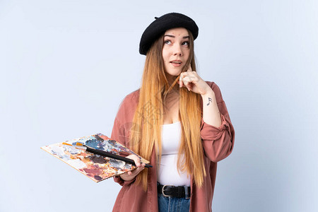 年轻女艺术家拿着一个调色板孤立在蓝背景思背景图片