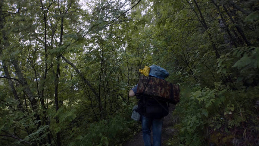 背着包走在森林小径上的旅行者的后视图影视素材在多云的天气里图片