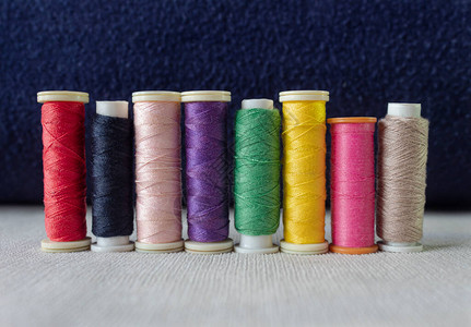 接近白纺织品和深蓝背景的八条多彩缝纫线时装和纺织概念Tymeandt图片
