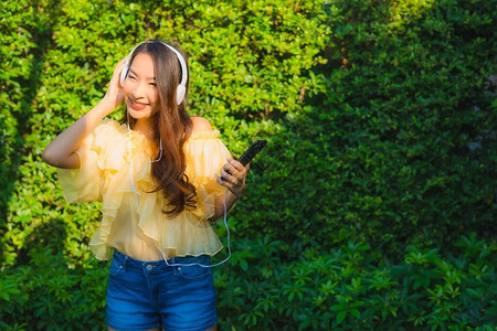年轻的亚洲女使用智能手机和耳机在户外花园自然观旁听音图片