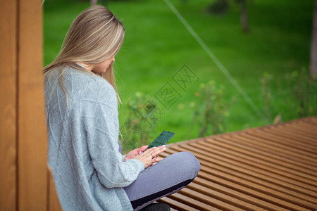 金发女孩坐在长凳上双腿坐着看智能手机图片