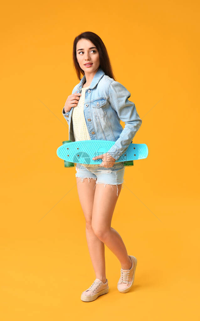 在彩色背景上带滑板的酷年轻女人图片