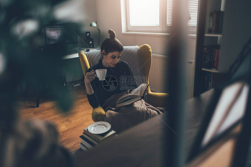 年轻读者用扶手椅拿着茶杯在家里看图片