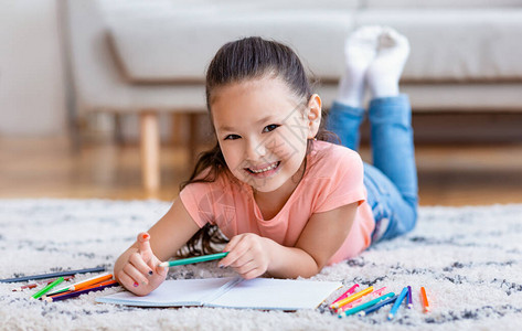 可爱的小女孩绘画手笔微笑到地板上图片