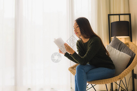肖像美丽的亚洲年轻女读书坐在客厅图片