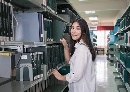 年轻的亚洲女人从图书馆架上拿书图片