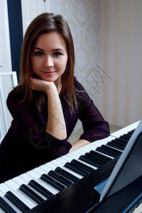 年轻女子坐在家里弹奏电子钢琴图片