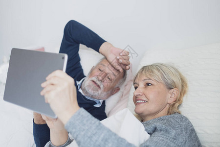 快乐的老年夫妇白种人老在卧室的白毯上使用平板电脑与家人开会图片