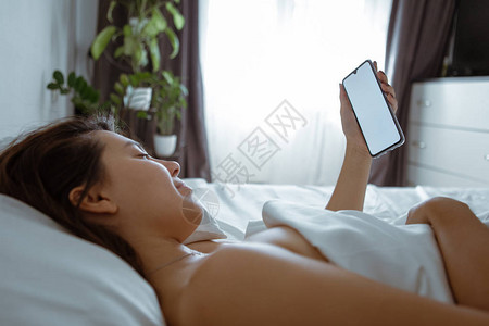 带智能手机的女人躺在床上图片