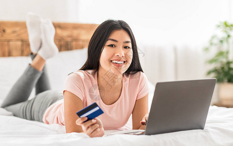 网上购物女孩拿着信用卡在家里用笔记本电脑在网上购物和购物图片