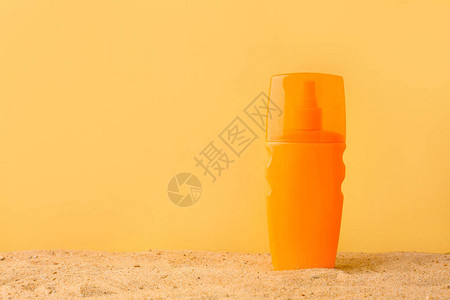 彩色背景下沙子上的防晒霜瓶背景图片
