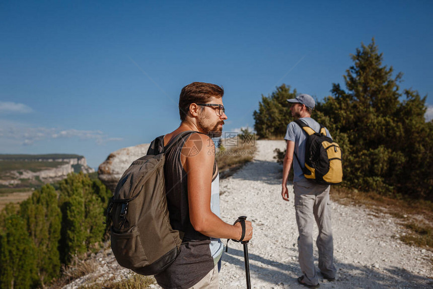 两名男子用登山杖背着包走在石坡上人们旁边的山谷视图夏天去大自然旅行背景中图片