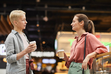 两个女人站在商场里一边聊天一边喝咖啡图片