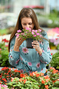 身穿长袖衬衫闻着粉红色花朵而围着满是鲜花的模糊植图片