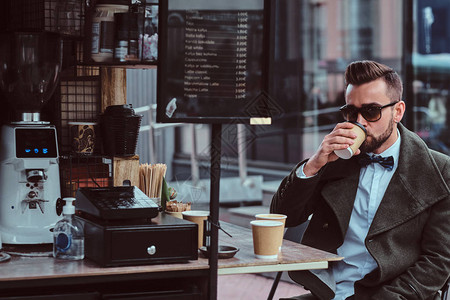 太阳镜里有魅力的优雅男子坐在咖啡店外边喝咖啡图片