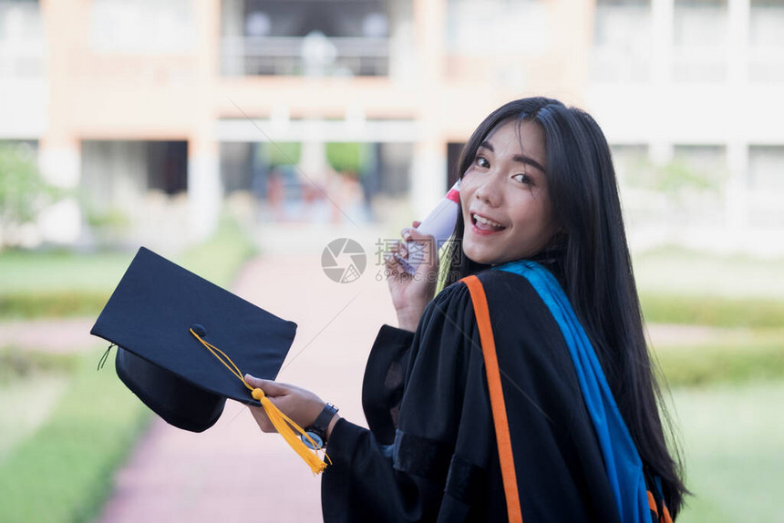 快乐和兴奋的年轻亚洲女大学毕业生的肖像在毕业典礼当天在大学校园里穿着毕业礼服和帽子庆祝学图片