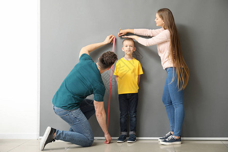 父母在灰墙附近测量儿子的身高图片