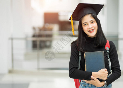 对持有背包书和戴毕业帽子的女青少年大学生的肖像代表了毕业概念教育版照片校对背景图片