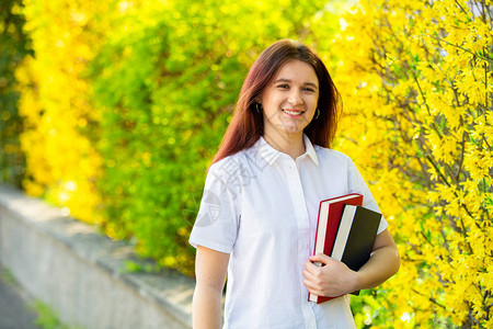 女大学生的微笑肖像在校园里户外拿着书看着相机一个自信的学生在大学建筑图片