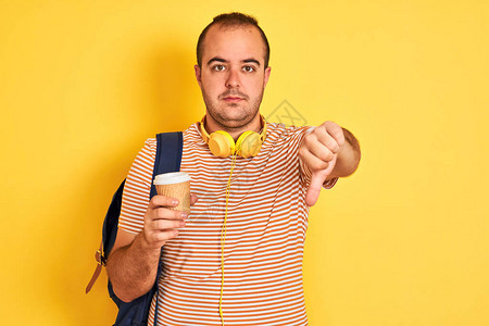 穿着背包耳机的学生男子在孤立的黄色背景上喝咖啡图片