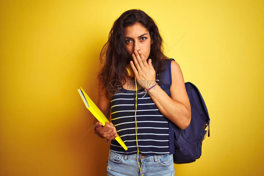 女学生在孤立的黄色背景面罩上戴bakcackpack笔记本耳机图片