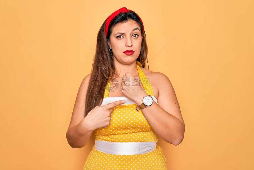 黄色背景中身穿时尚感50年代风格的年轻西班牙裔别针女人急着指点看时间图片