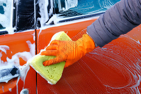 戴橡皮手套的人用黄色海绵洗其橙色汽车图片