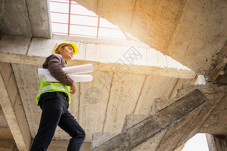 在房屋建筑工地手头戴防护头盔和图纸的年轻专业工程师图片