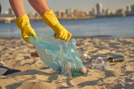 戴着黄色手套的负责任的家伙带着垃圾袋沿着肮脏的河边走图片