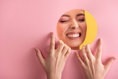 粉红纸圆洞中闪亮化妆的美丽女肖像显示黄色图片