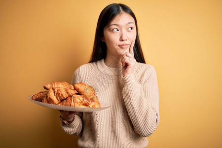 年轻的亚洲女拿着法式糕点羊角面包图片