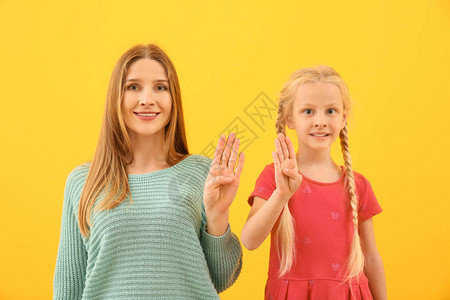 小聋哑女孩和母亲在彩色背景上使用手语的失图片
