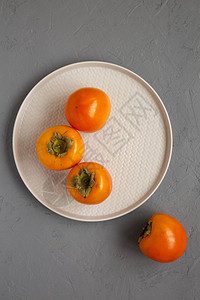 灰色表面上的盘子上的生熟橙柿子图片