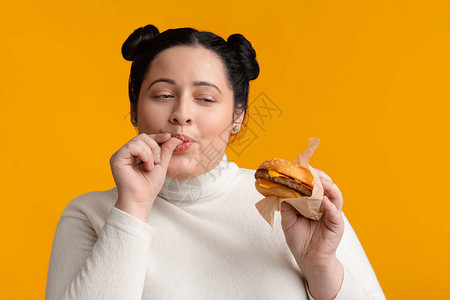 年轻的胖女孩吃芝士汉堡三明治和舔手指有食欲背景图片