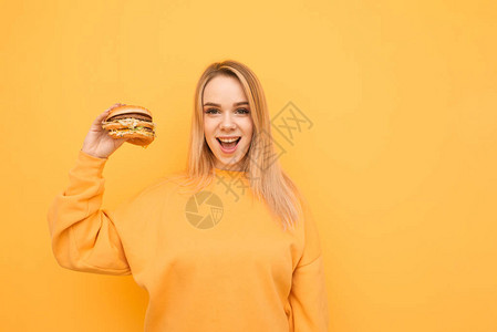 快乐的女孩手里拿着一个黄色背景的汉堡图片