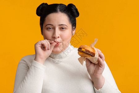 年轻肥胖女孩吃汉堡和舔手指享受快餐高图片