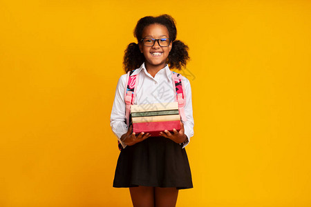 令人兴奋的非裔美国一年级女生在工作室里持有黄背景书籍堆积于黄背景中背景图片