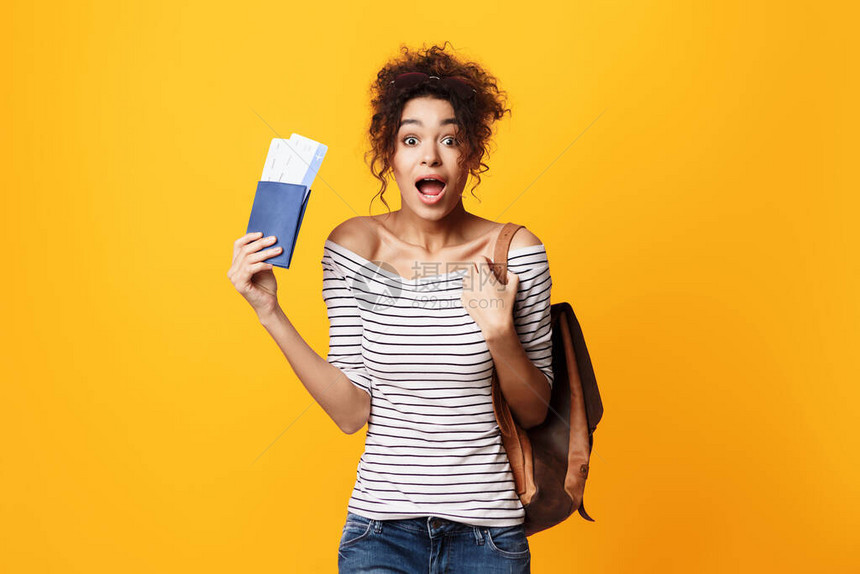 放假时间兴奋的非洲旅游女孩拿着票站在黄色背景图片