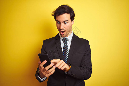 年轻英俊的商人用智能手机站在与世隔绝的黄色背景上图片