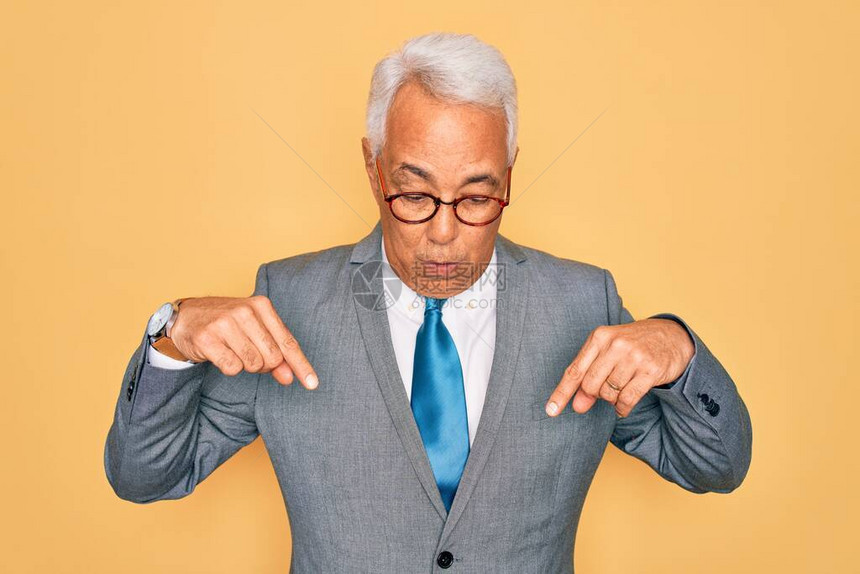 身戴黄色眼镜的灰色头发英俊高级商人用手指向下指图片