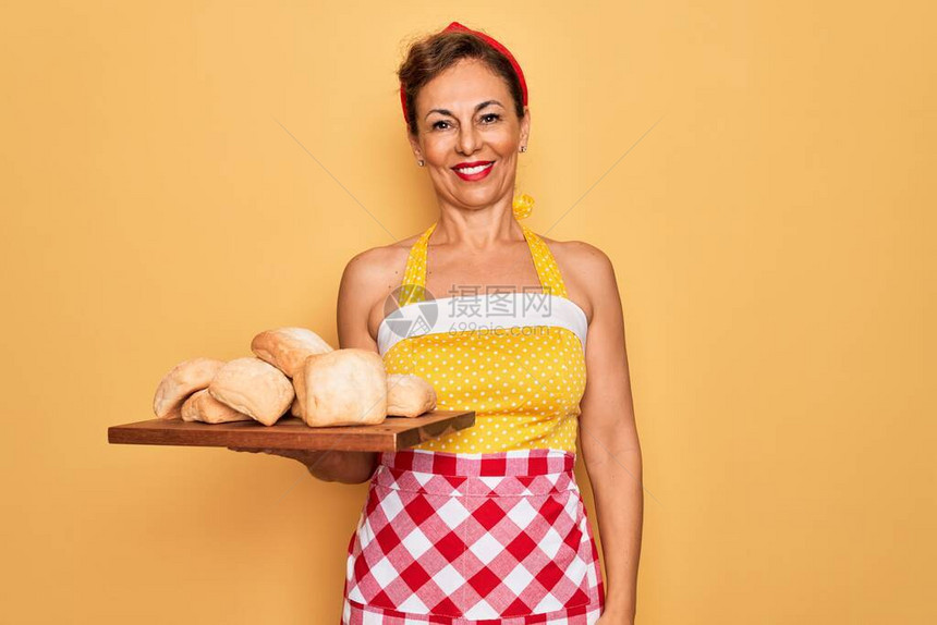 中年高级家庭主妇穿着50年代风格的复古连衣裙和围裙烹饪面包图片