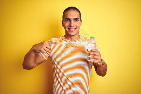 年轻帅哥拿着塑料水瓶在黄色孤立的背景下非常高兴地用图片