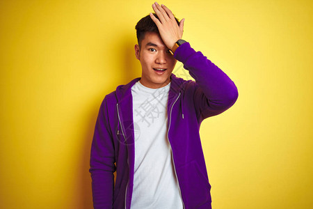 身穿紫色运动衫的年轻亚洲华裔男子站在孤立的黄色背景上图片